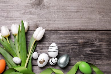 Many painted Easter eggs, tulip flowers and ribbon on wooden table, flat lay. Space for text