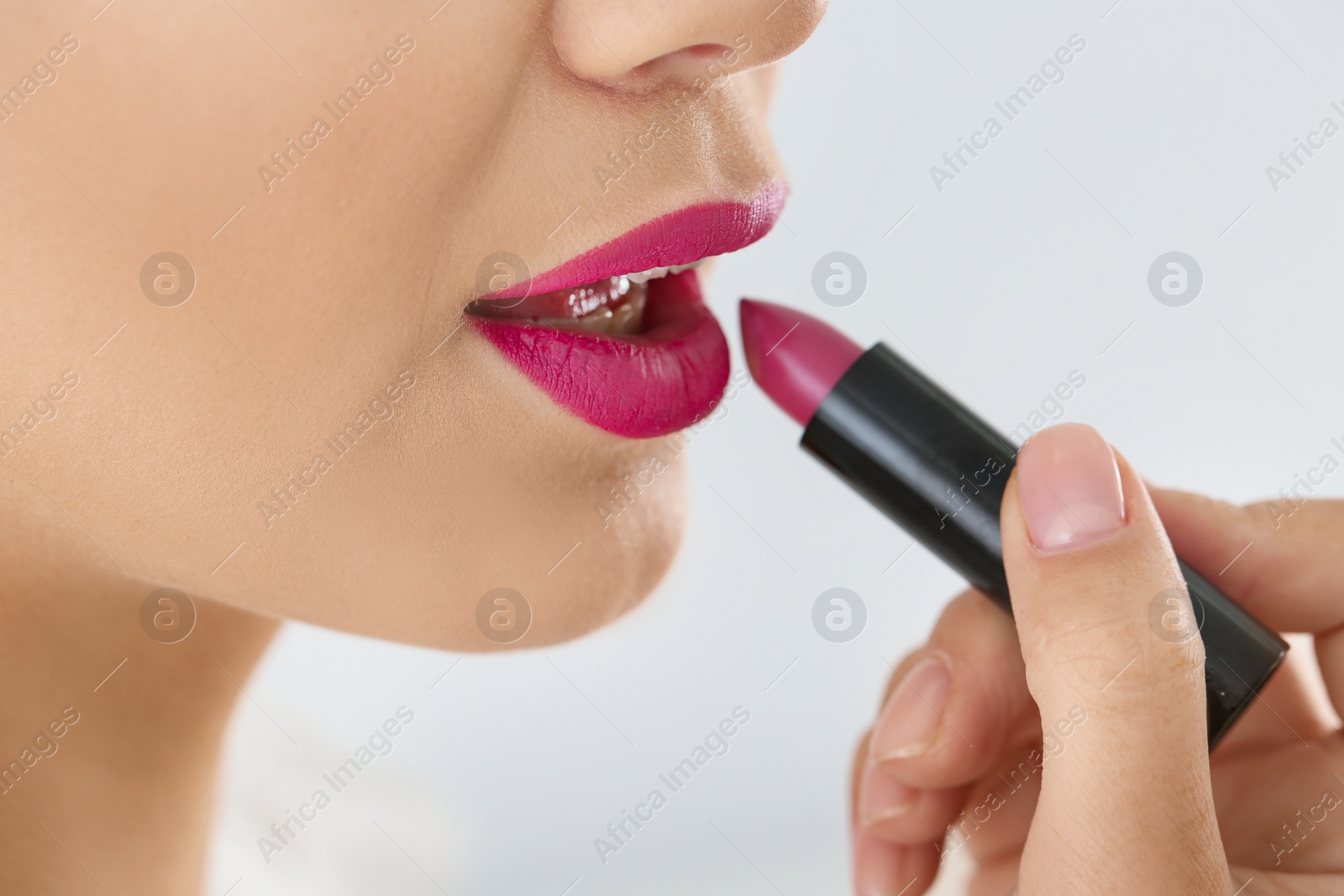 Photo of Beautiful woman applying lipstick on light background, closeup