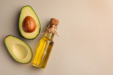 Photo of Glass bottlecooking oil and fresh avocados on light grey background, flat lay. Space for text