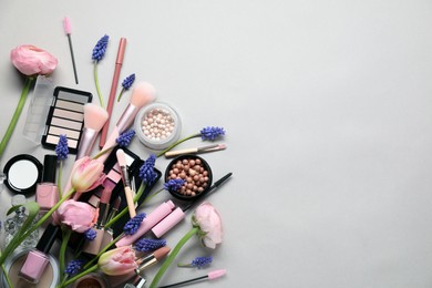 Flat lay composition with different makeup products and beautiful spring flowers on gray background, space for text