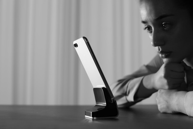 Lonely woman with mobile phone at table indoors, space for text. Black and white effect