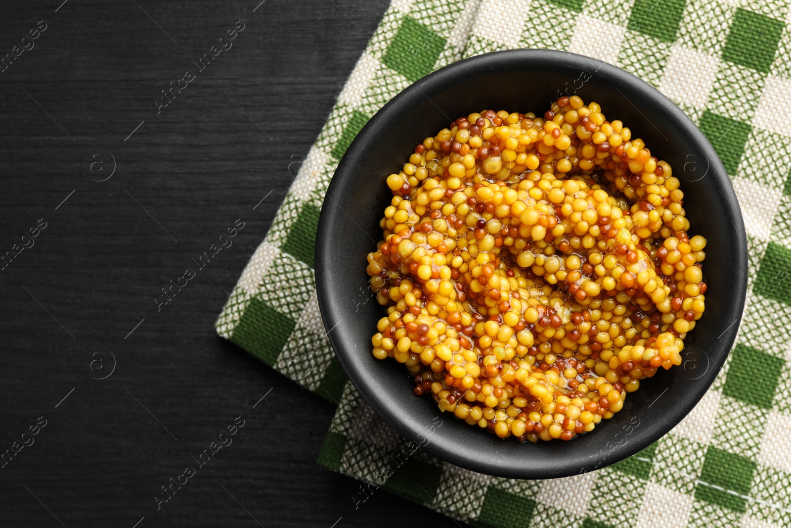 Photo of Whole grain mustard in bowl on black wooden table, top view. Space for text