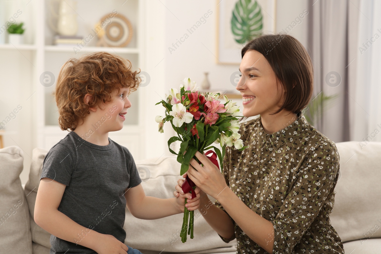 Photo of Happy woman with her cute son and bouquet of beautiful flowers at home. Mother's day celebration