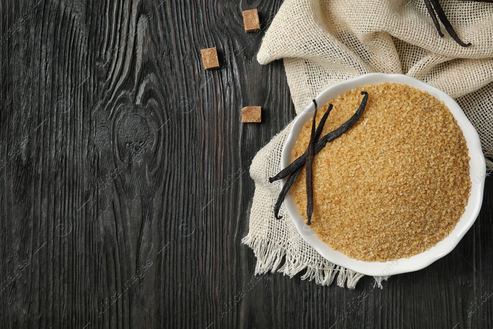 Photo of Bowl with brown vanilla sugar on wooden background, top view