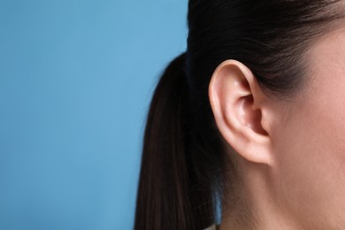 Photo of Woman on light blue background, closeup of ear. Space for text