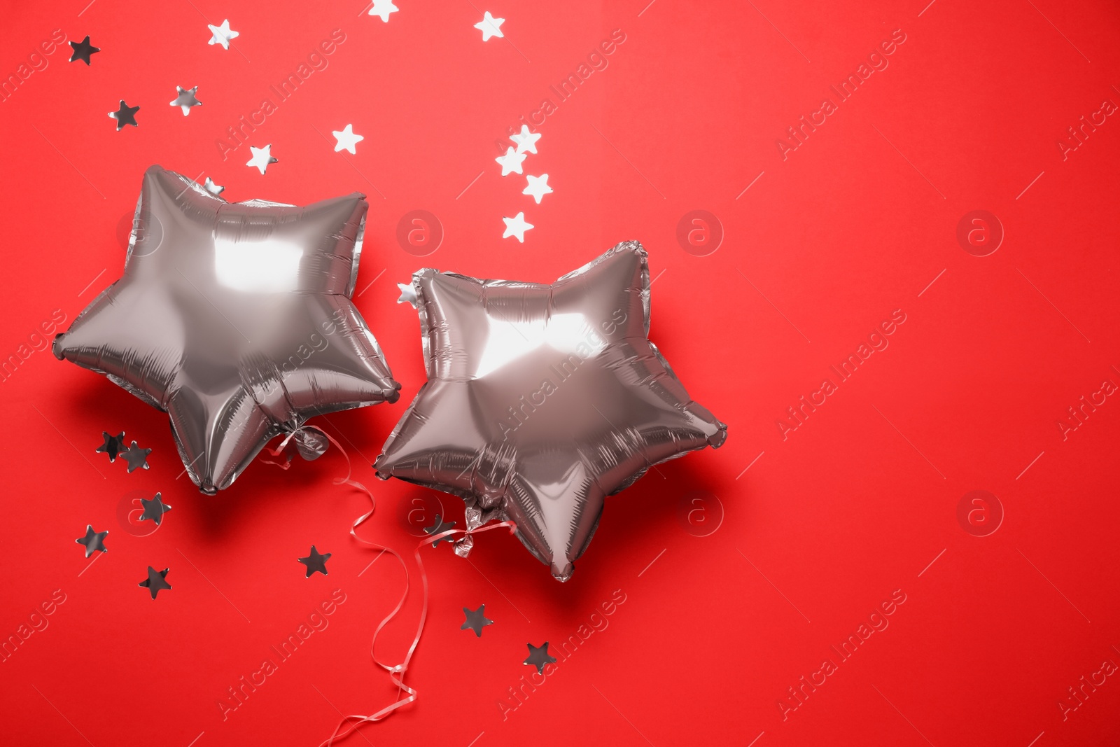 Photo of Star shaped pink balloons and confetti on red background, flat lay