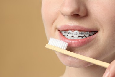 Photo of Woman with dental braces cleaning teeth on beige background, closeup. Space for text