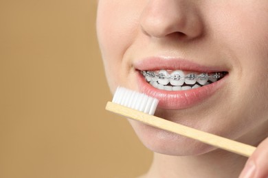 Woman with dental braces cleaning teeth on beige background, closeup. Space for text