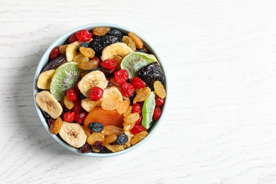 Bowl of different dried fruits on wooden background, top view with space for text. Healthy lifestyle