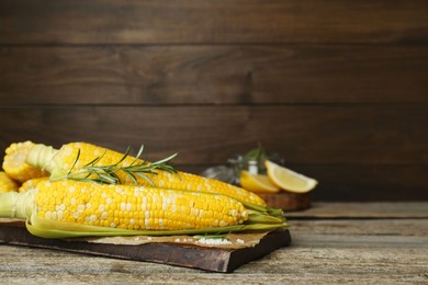 Photo of Tasty cooked corn cobs on wooden table, space for text