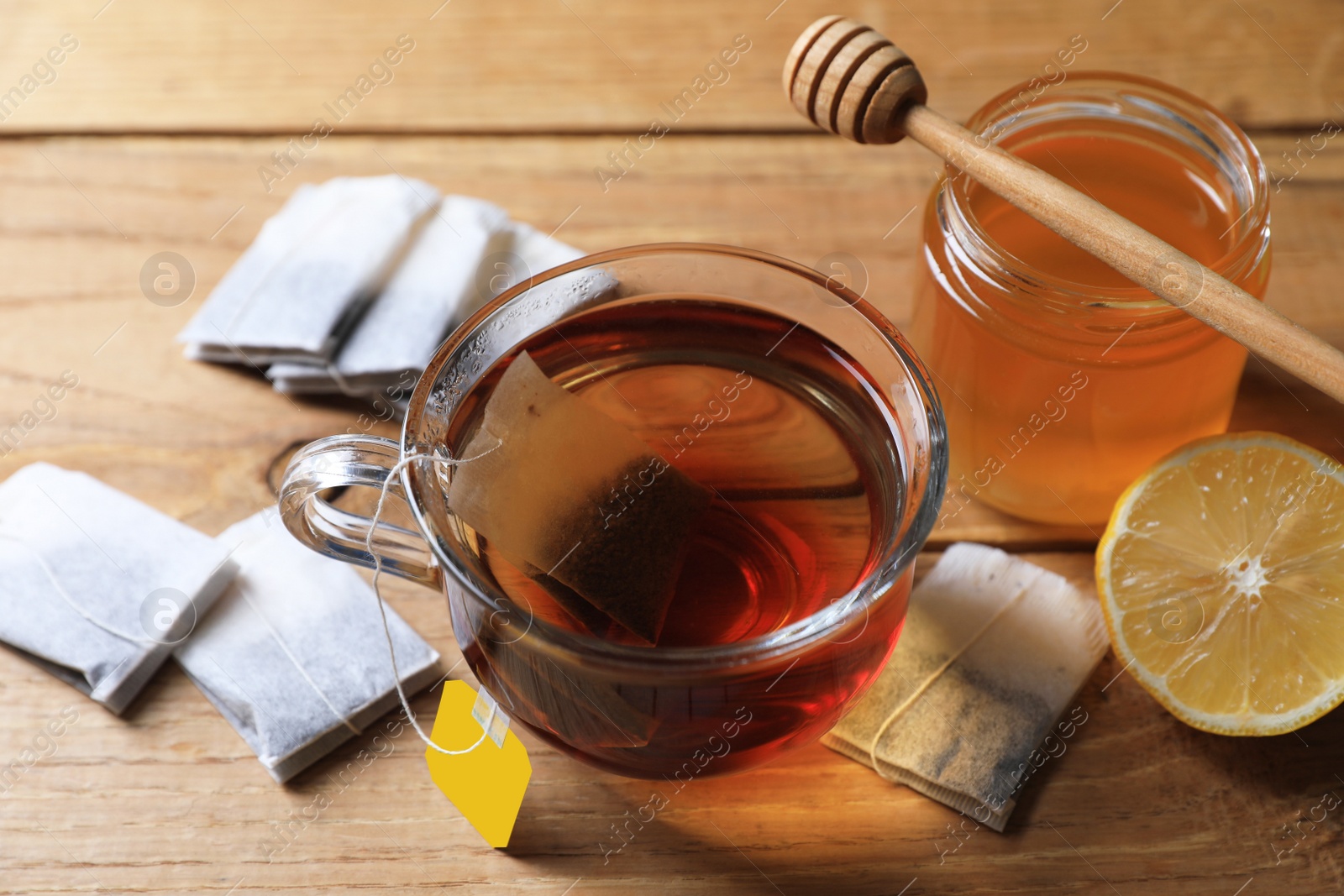 Photo of Tea bag in glass cup, honey and lemon on wooden table