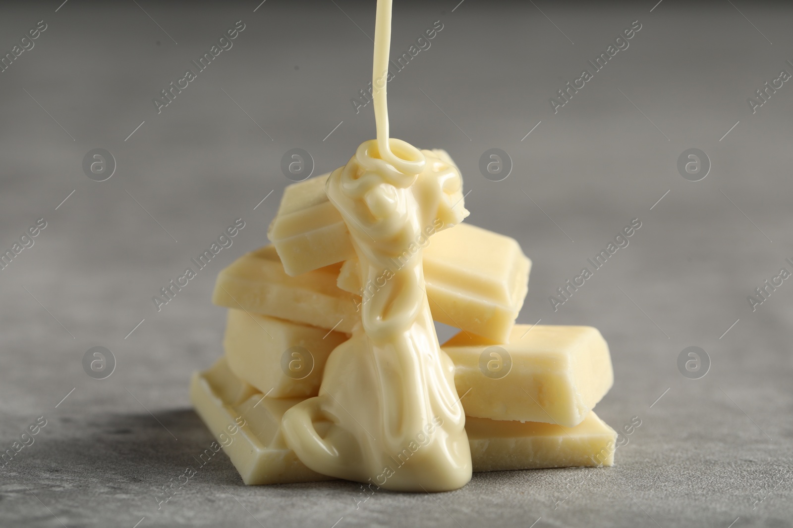 Photo of Pouring tasty white chocolate paste onto pieces on grey table, closeup