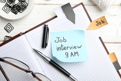 Photo of Reminder note about job interview and stationery on table, flat lay