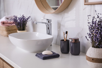Photo of Bathroom counter with vessel sink, accessories and flowers. Interior design