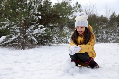 Photo of Cute little girl rolling snowballs in winter forest