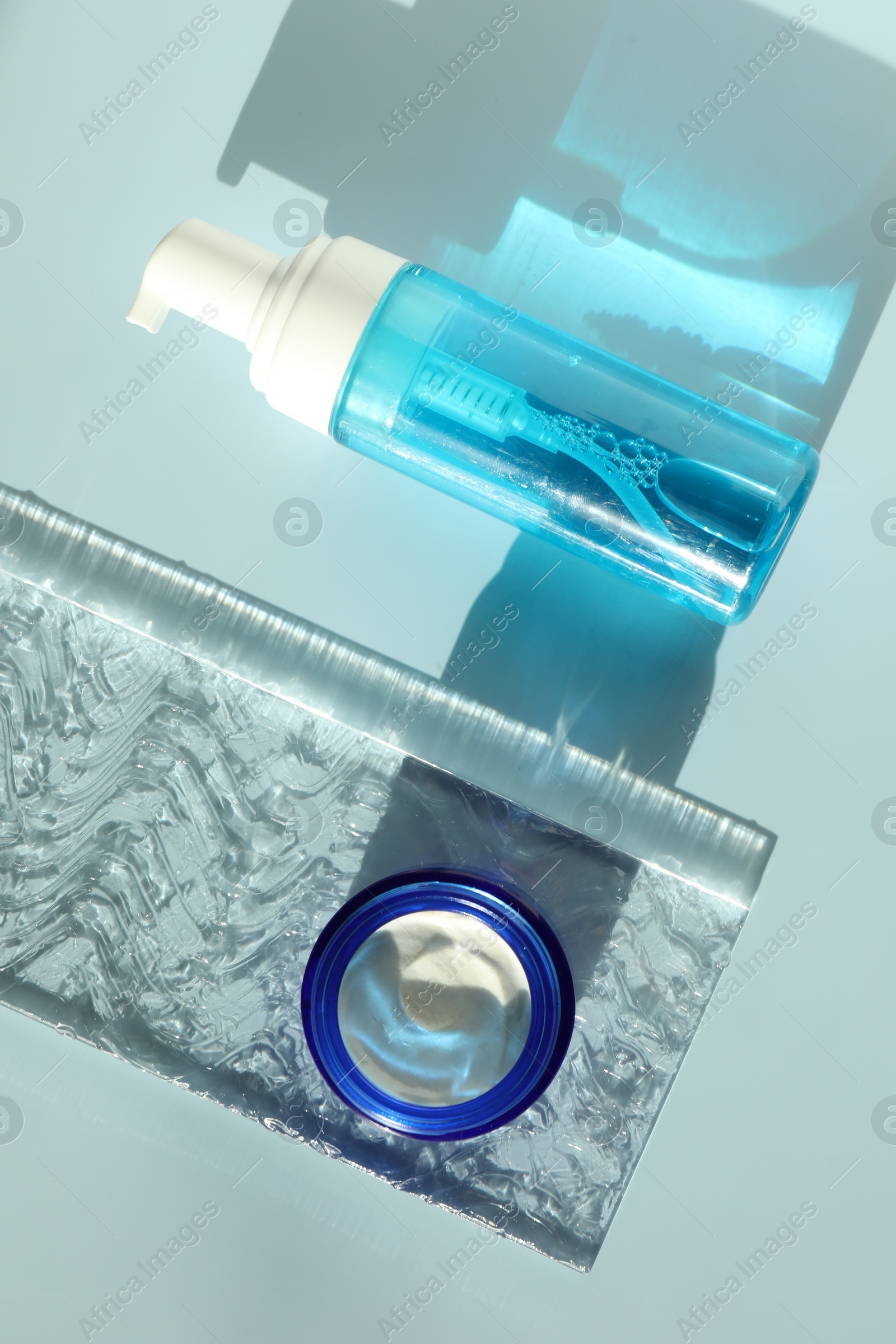 Photo of Bottle and jar of cosmetic products on light blue background, flat lay