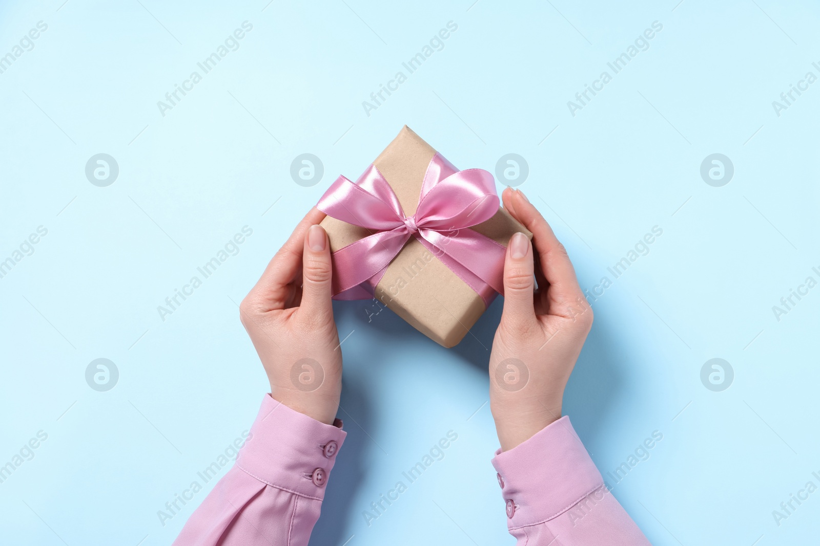 Photo of Woman holding gift box with pink bow on light blue background, top view
