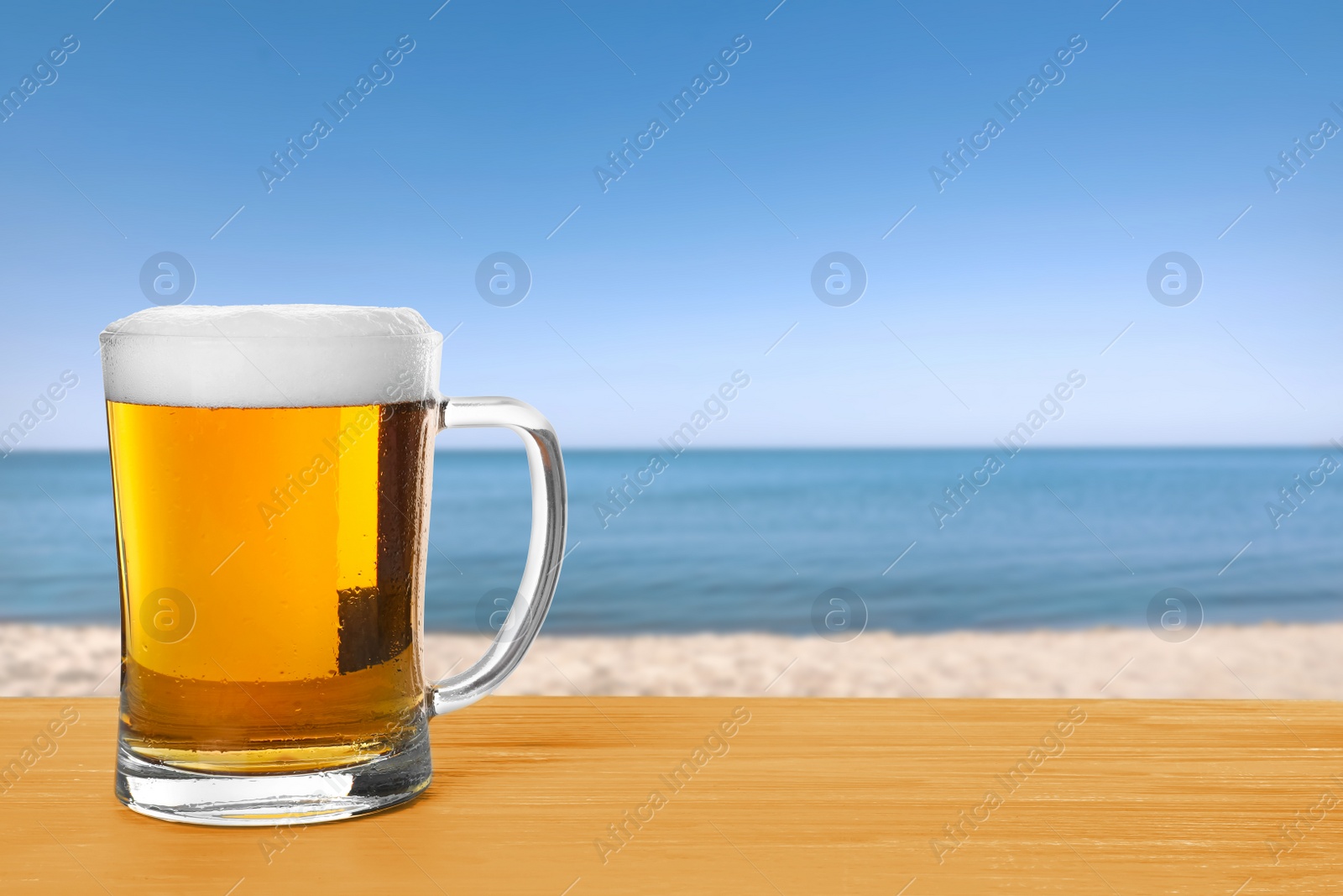 Image of Cold beer on wooden desk against blurred sea. Space for text