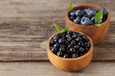 Photo of Ripe bilberries and leaves in bowls on wooden table, closeup. Space for text