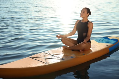 Young meditating yoga on color SUP board on river at sunset