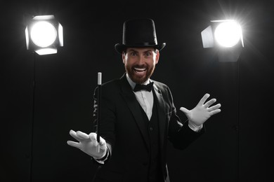 Photo of Happy magician in top hat holding wand on stage