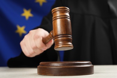 Photo of Judge with gavel at wooden table against flag of European Union, closeup