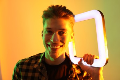 Young man with square lamp on color background in neon lights