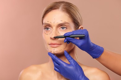 Doctor with marker preparing patient for cosmetic surgery operation on light brown background