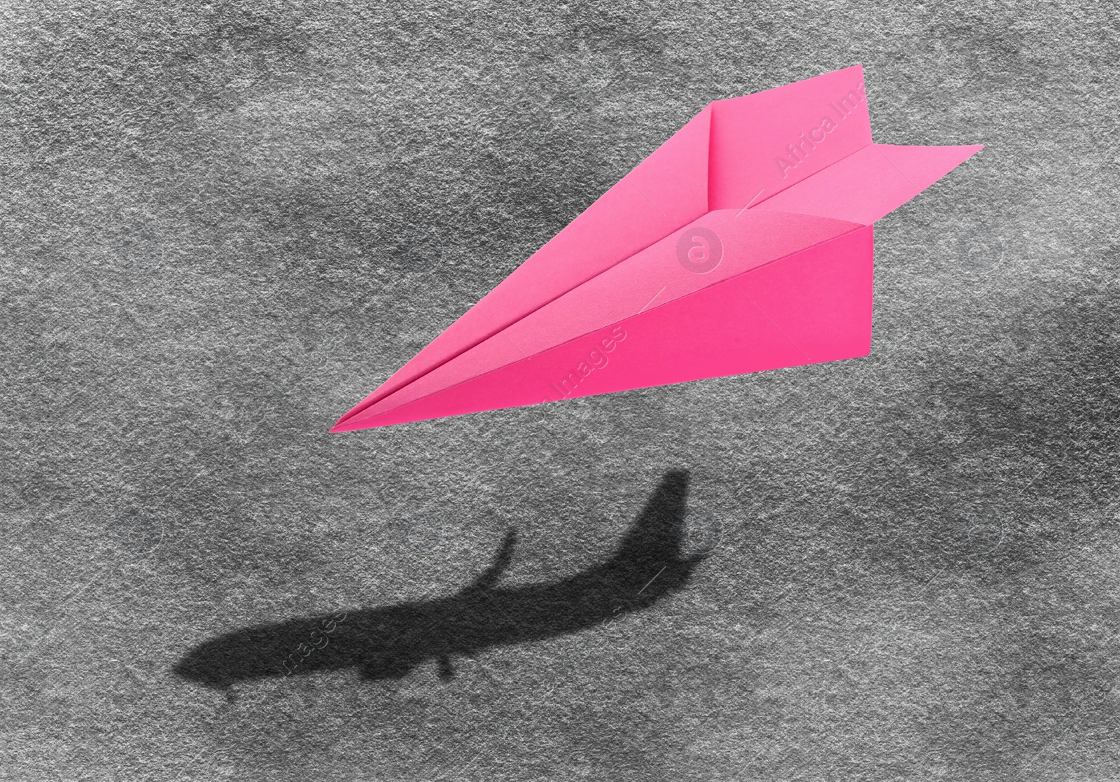 Image of Flying paper plane and shadow of a real airplane on asphalt