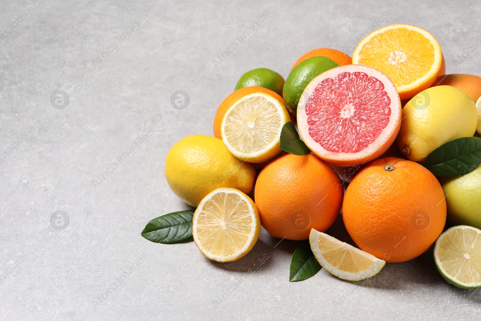 Photo of Pile of different fresh citrus fruits and leaves on grey textured table, closeup. Space for text