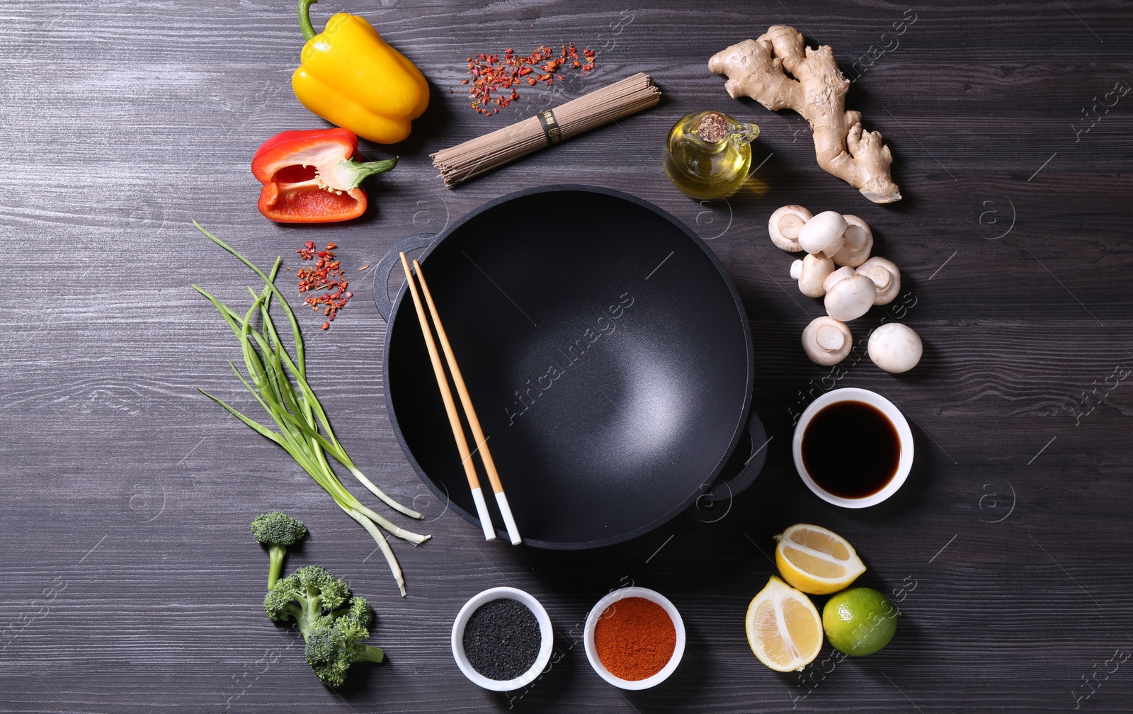 Photo of Empty iron wok and chopsticks surrounded by ingredients on dark grey wooden table, flat lay