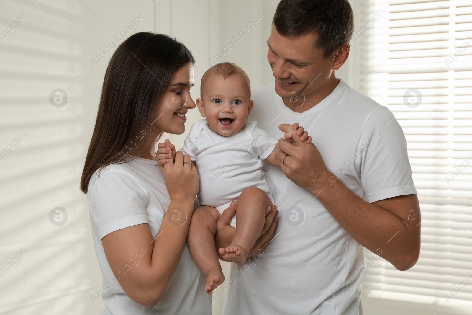 Photo of Happy family. Couple with their cute baby near window indoors