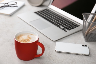 Red cup with coffee and phone near laptop on office table. Break time