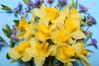 Photo of Bouquet of beautiful yellow daffodils and periwinkle flowers on light blue wooden table, top view