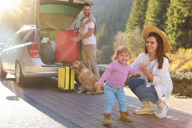 Photo of Mother with her daughter, man and dog near car outdoors. Family traveling with pet