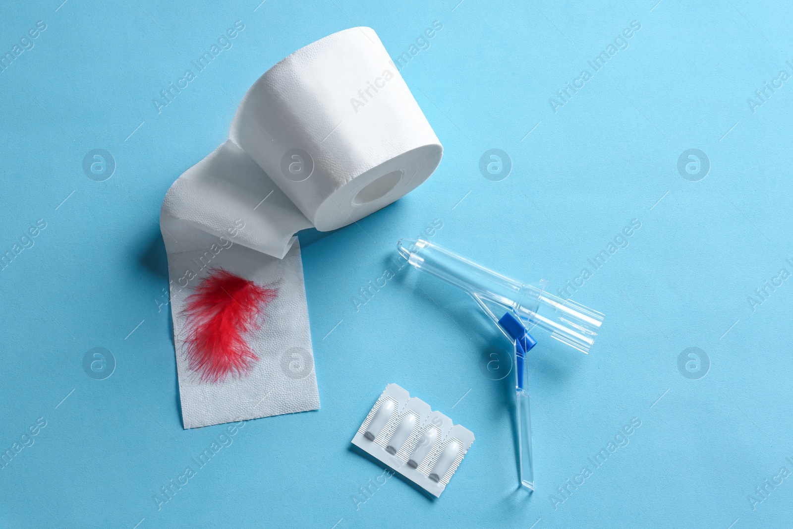 Photo of Anoscope, suppositories and toilet paper with red feather on light blue background, flat lay. Hemorrhoid treatment