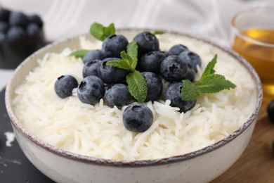 Photo of Bowl of delicious rice porridge with blueberries and mint on table, closeup