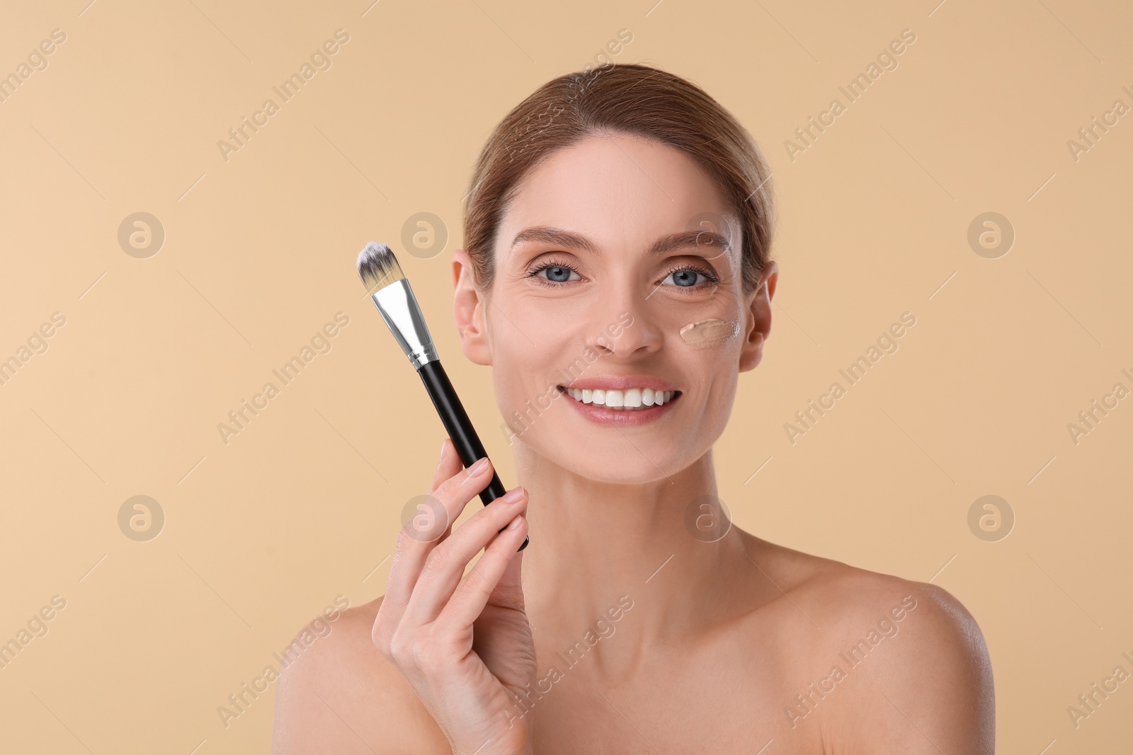 Photo of Woman with swatch of foundation holding makeup brush on beige background