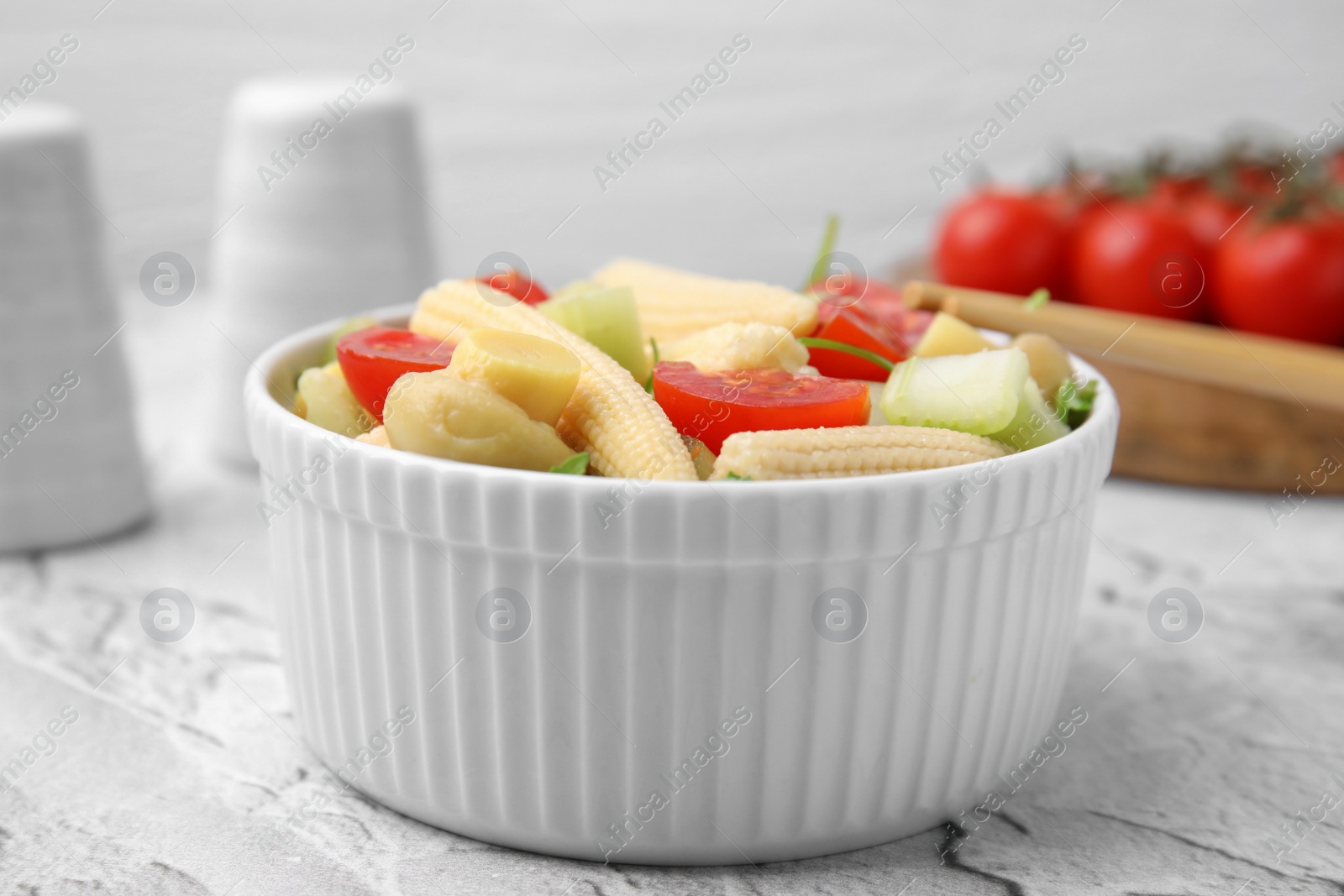 Photo of Tasty baby corn with vegetables and champignons on grey textured table, closeup