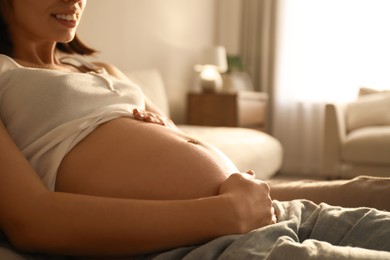 Pregnant young woman touching belly at home, closeup