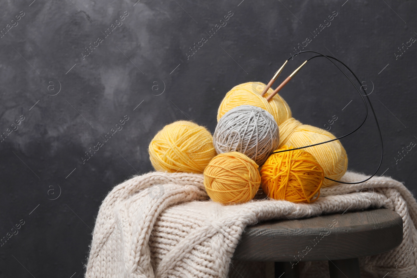 Photo of Woolen yarns with knitting needles and scarf on stand near black wall. Space for text