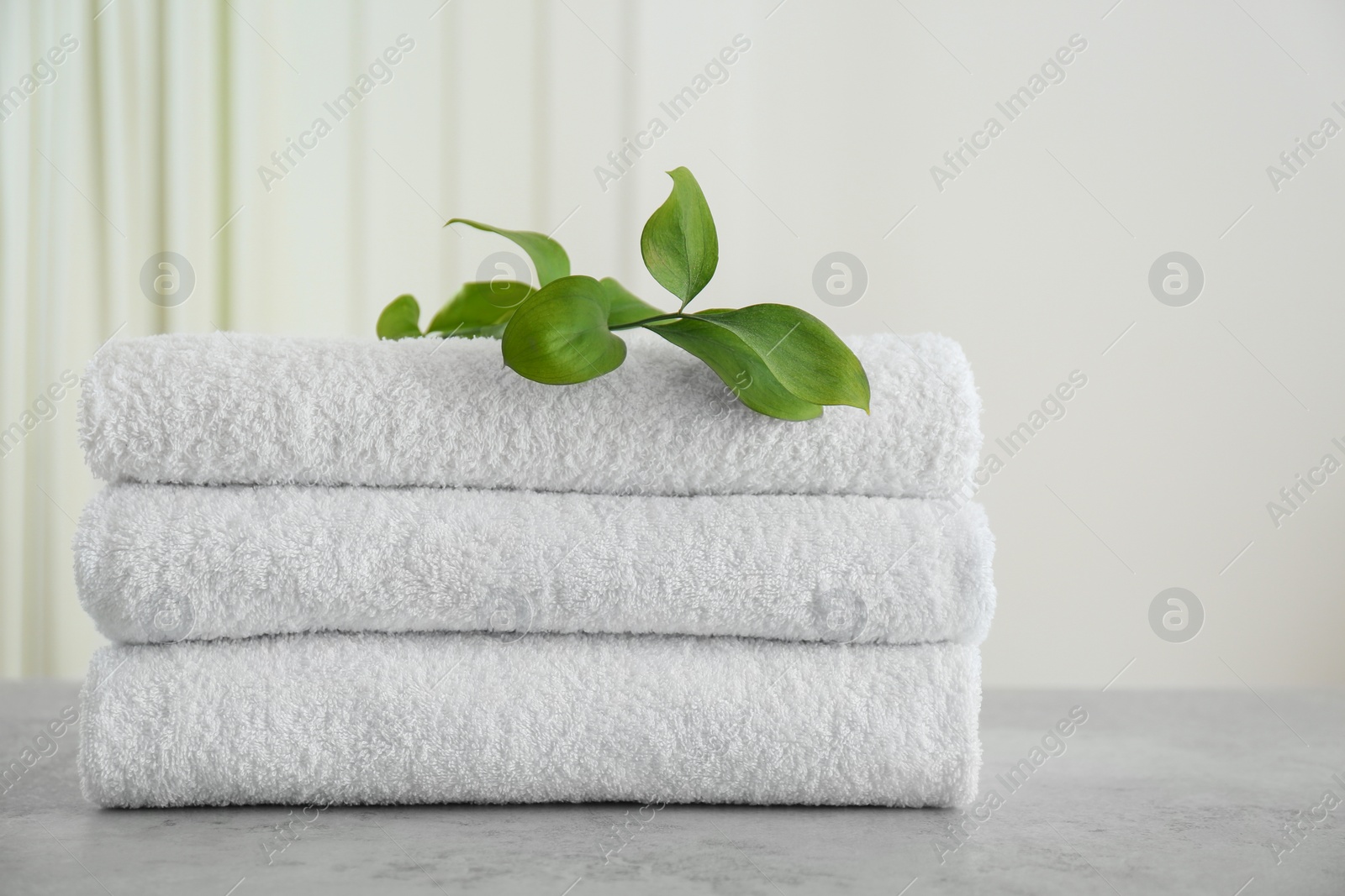 Photo of Fresh towels and green branches on light grey stone table in bathroom