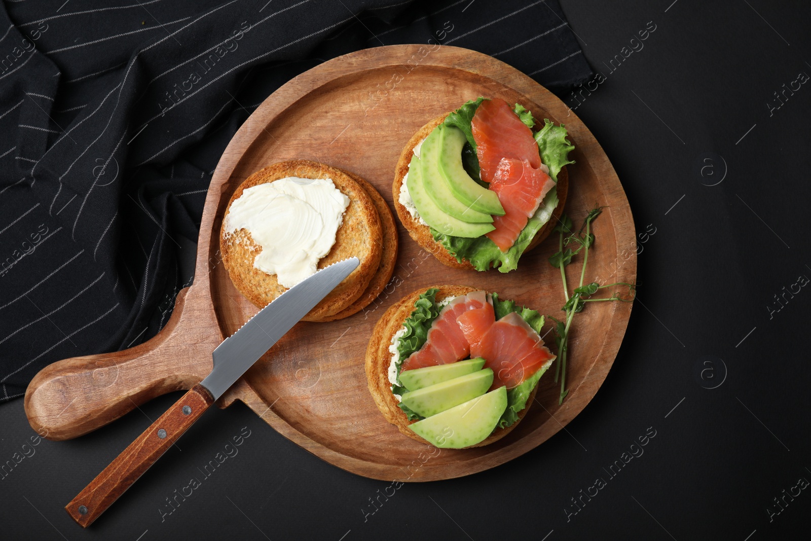 Photo of Tasty rusks with salmon, cream cheese and avocado served on black table, flat lay