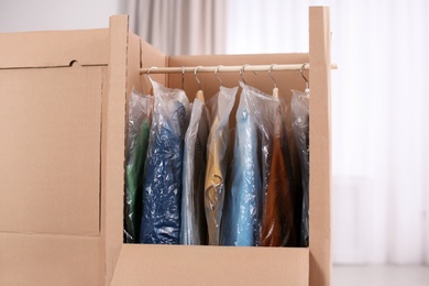 Photo of Cardboard wardrobe boxes with clothes on hangers indoors. Moving day