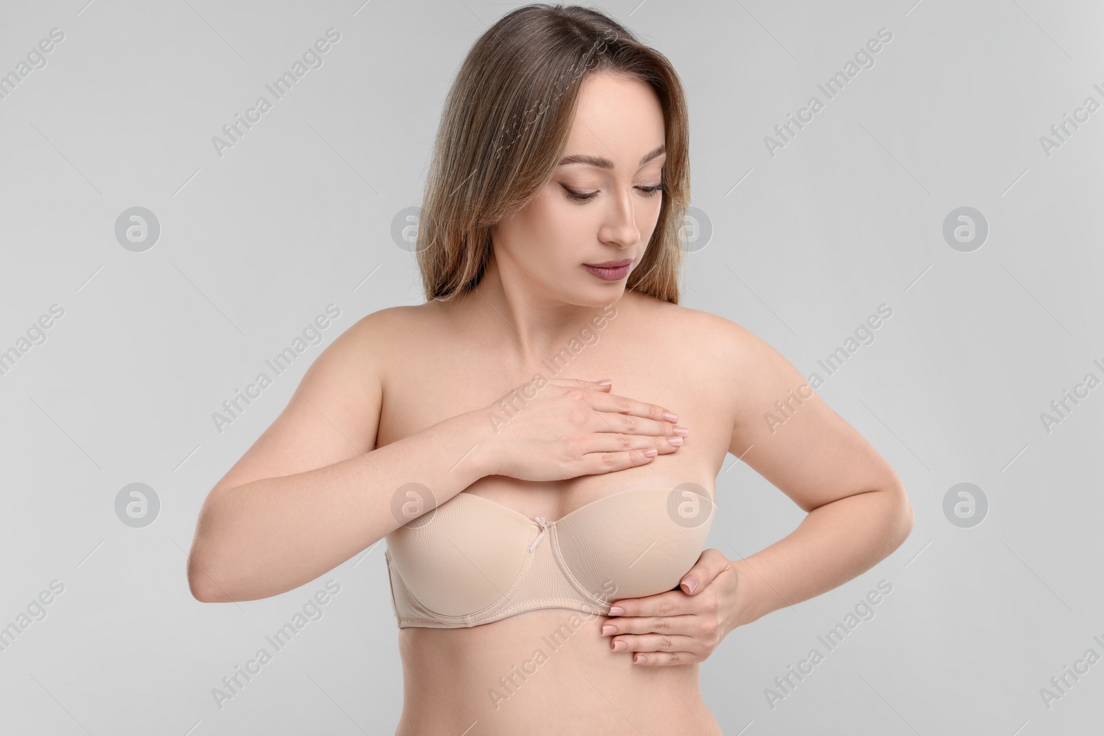 Photo of Mammology. Young woman doing breast self-examination on light grey background
