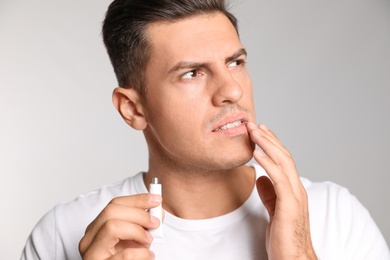 Man with herpes applying cream on lips against light grey background
