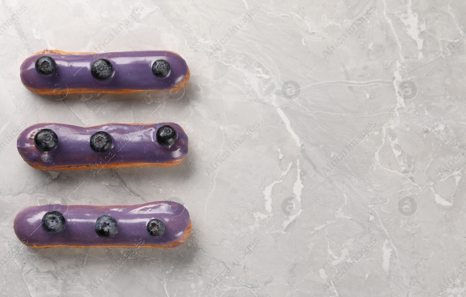 Photo of Tasty glazed eclairs with blueberries on grey marble table, flat lay. Space for text