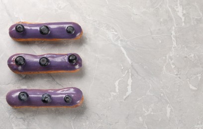 Tasty glazed eclairs with blueberries on grey marble table, flat lay. Space for text