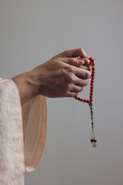 Photo of Muslim man with misbaha praying on light grey background, closeup