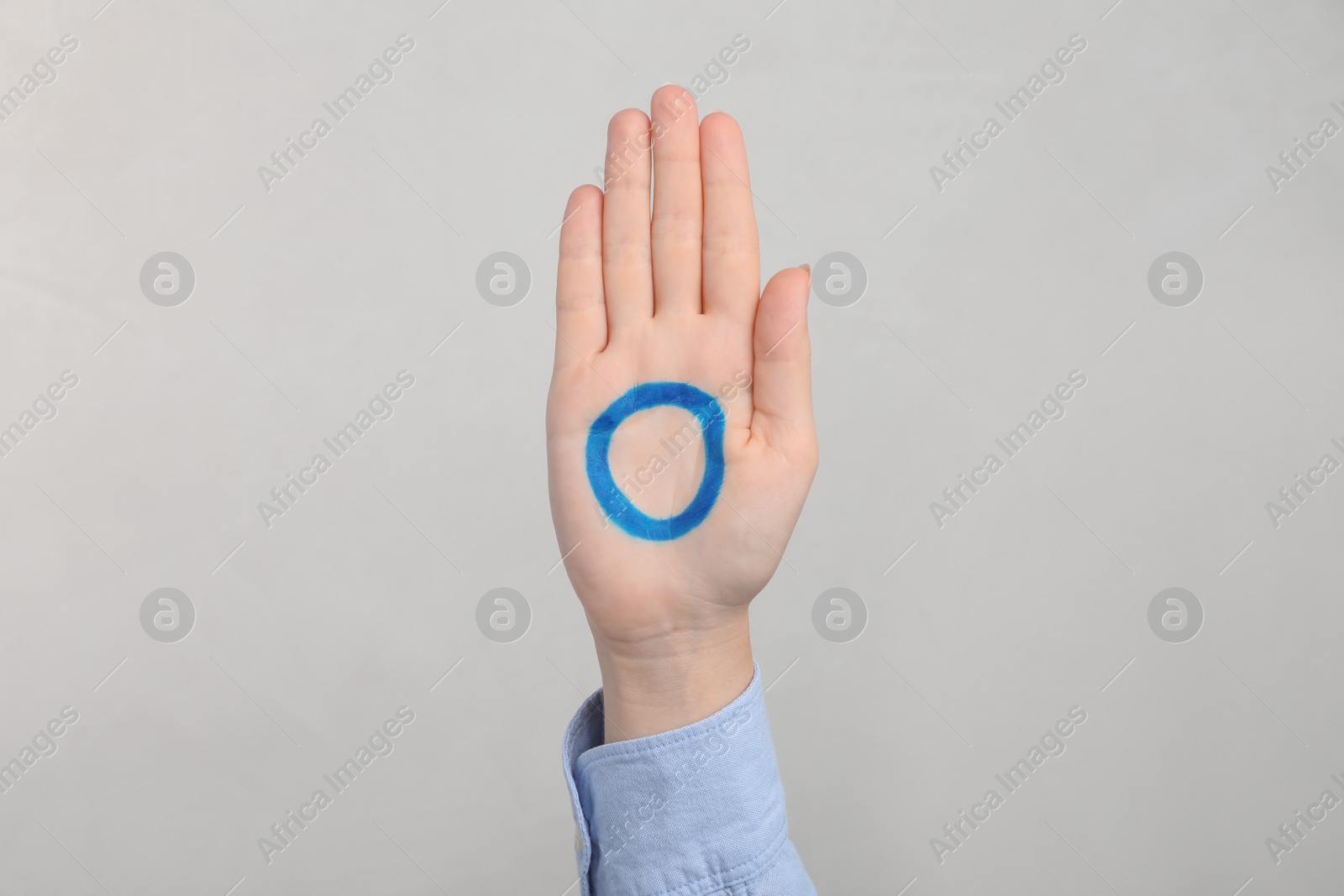 Photo of Woman showing blue circle drawn on palm against light grey background, closeup. World Diabetes Day